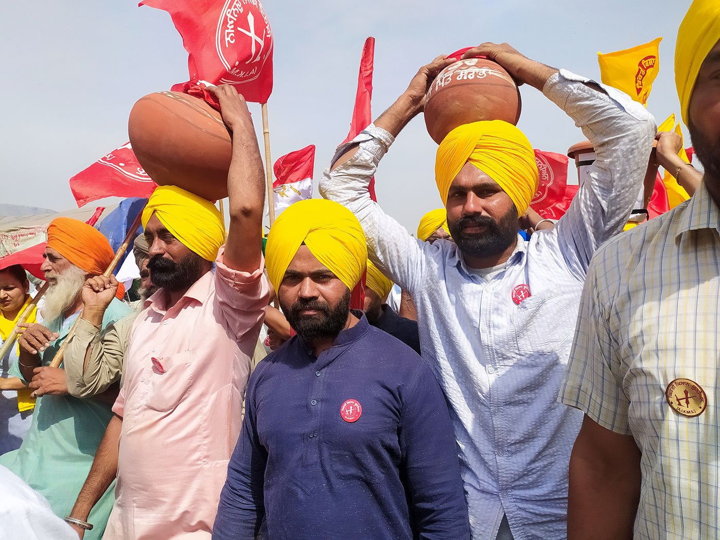 Young farmers carrying the pots on their heads as they walk to towards the stage at Singhu. Left: Supporters stand by