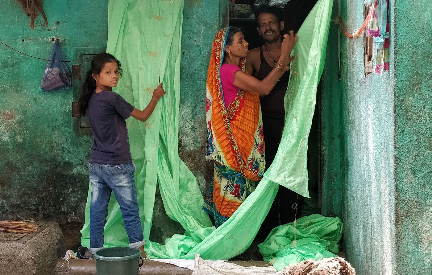 Shanti Sahu and her daughter Asha have fixed a rope outside their one room home in Mina Nagar to begin work on the saris that have been sent for the day. Shanti’s husband, Arijit, looks on.