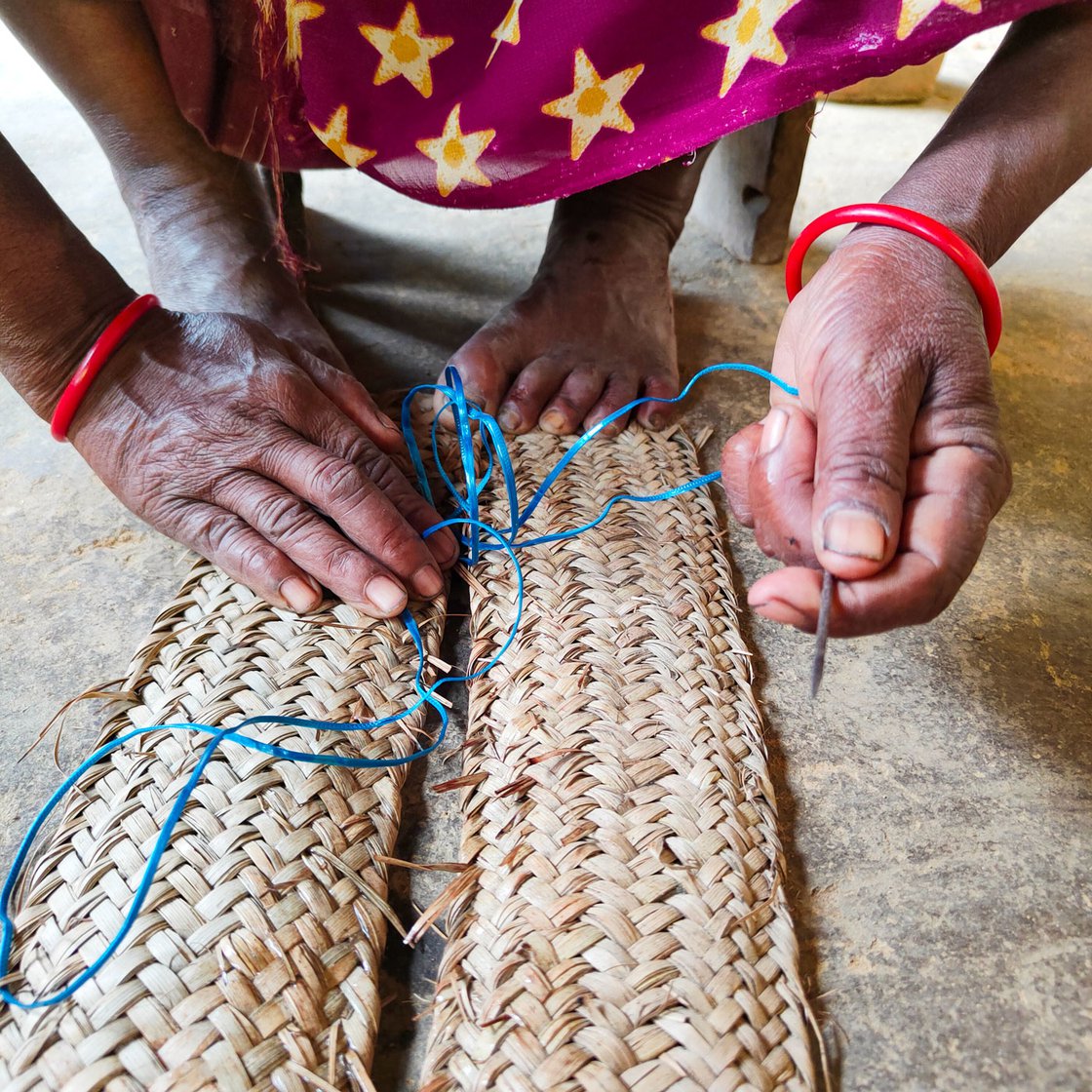 A long knife, a block of wood and a hammer help Jolen in achieving a clean cut. She uses a thick needle and plastic thread to stitch (right) the woven strips together