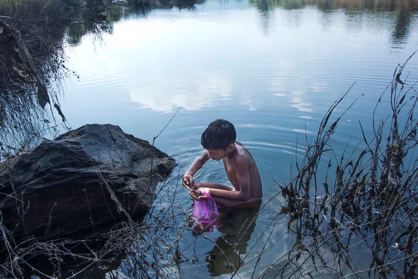 A young boy collects shellfish from the Subarnarekha river